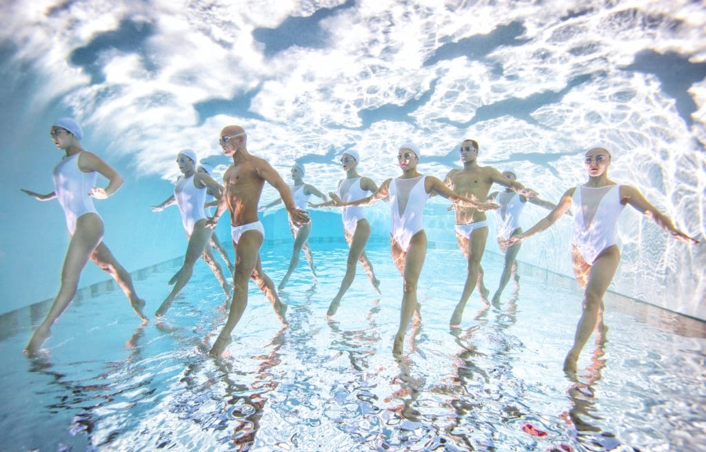 Ten synchronized swimmers standing under water.