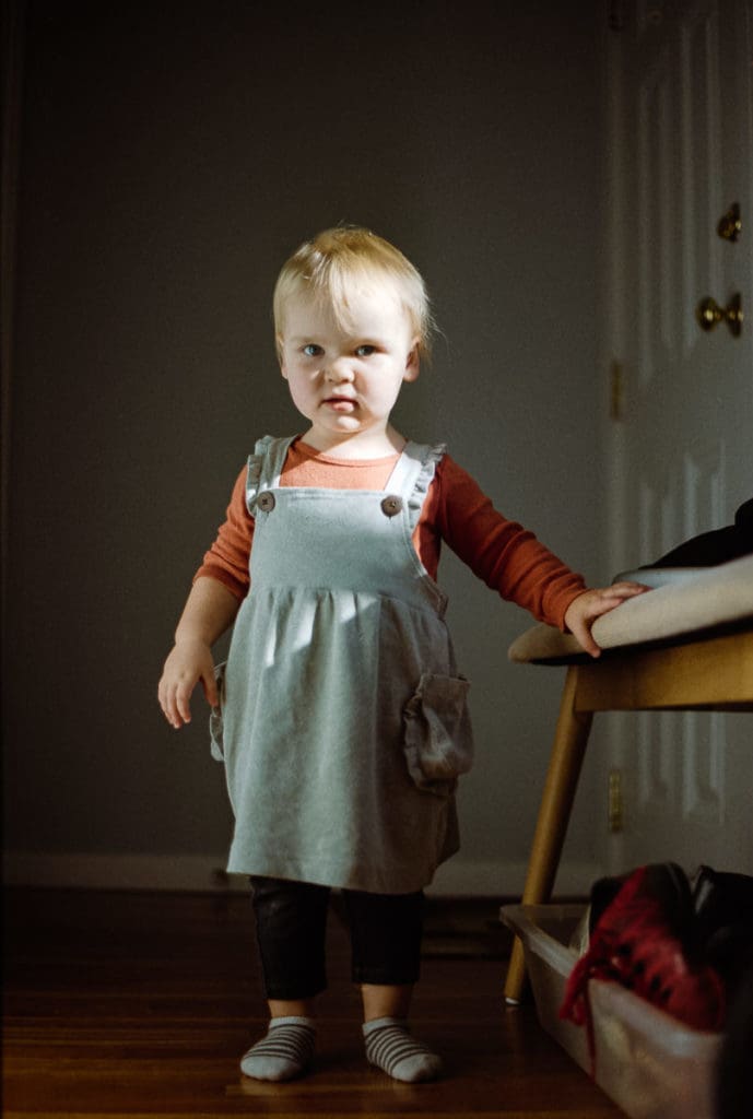 A film photograph of a little girl standing in a ray of window light