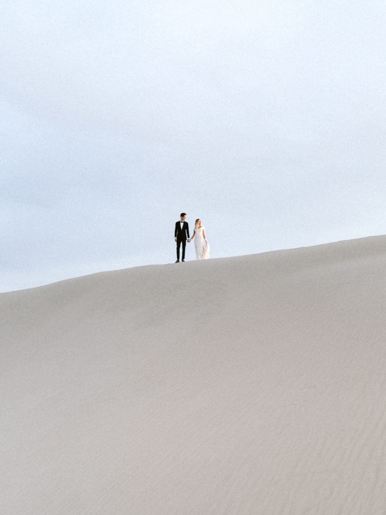 posing wedding couple in sun rays on sand dunes before light disappears by braden young