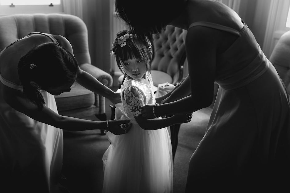 Flower girl captured in light and shadow as bridesmaids help her get ready.