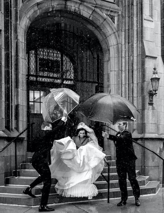 candid moment of bride under umbrellas going to car.