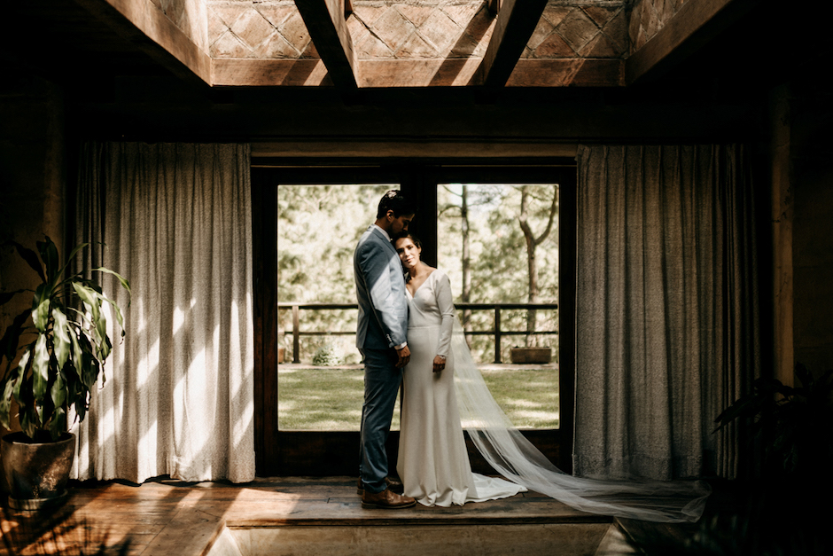moment of tranquility in candid photo of bride and groom against window.