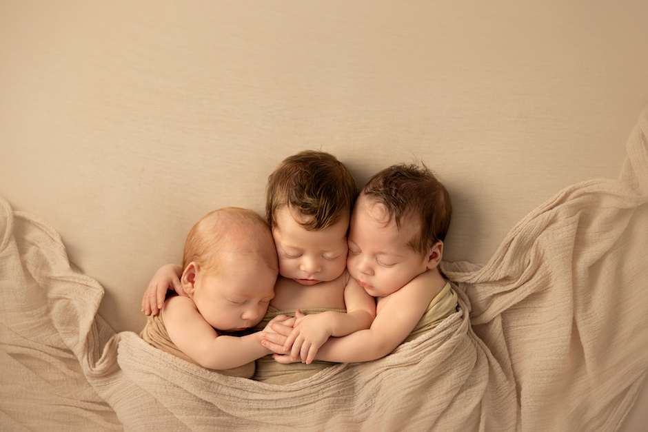 newborn triplets side by side and holding hands.