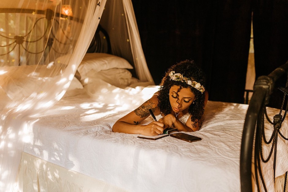 A bride on bed writing her wedding vows in directional light.