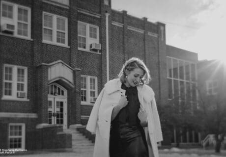 A black-and-white image of a woman outside a brick building, made using Lensbaby 50mm f/2.5 Soft Focus II.