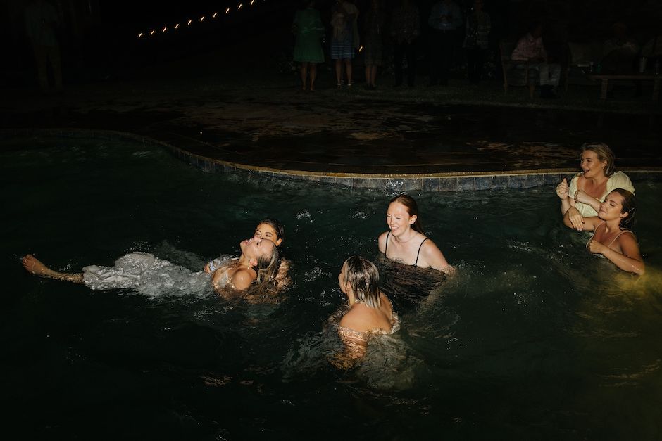 bridal party swimming in pool at night with photo lighting from across the pool.