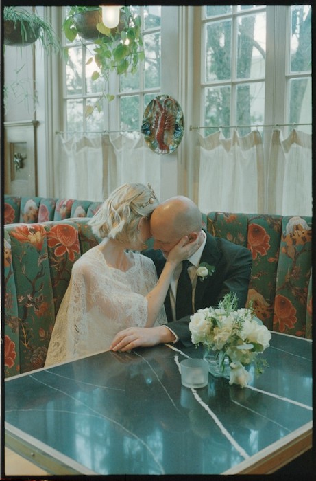 Bride and groom sitting in banquette with heads close together.