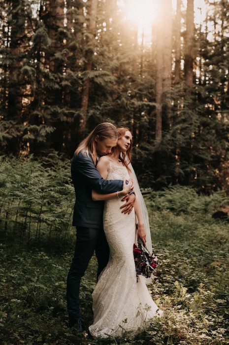 Bride and groom embrace in clearing in forest.