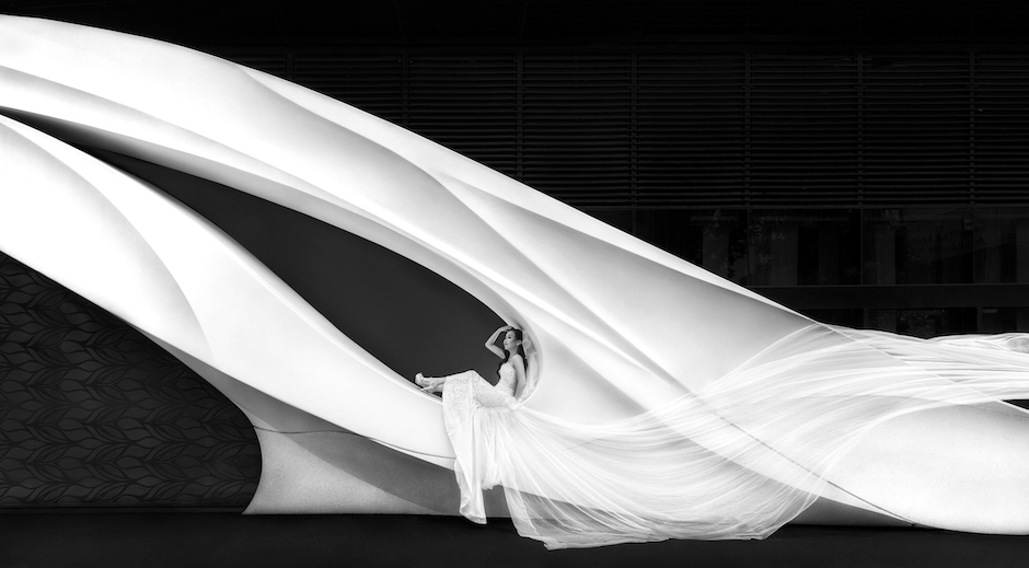 bride sits in curve of arch with veil spread out behind her.
