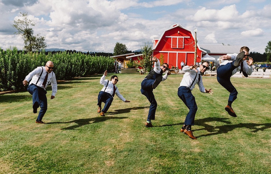 groomsmen doing a kick outside near red barn.