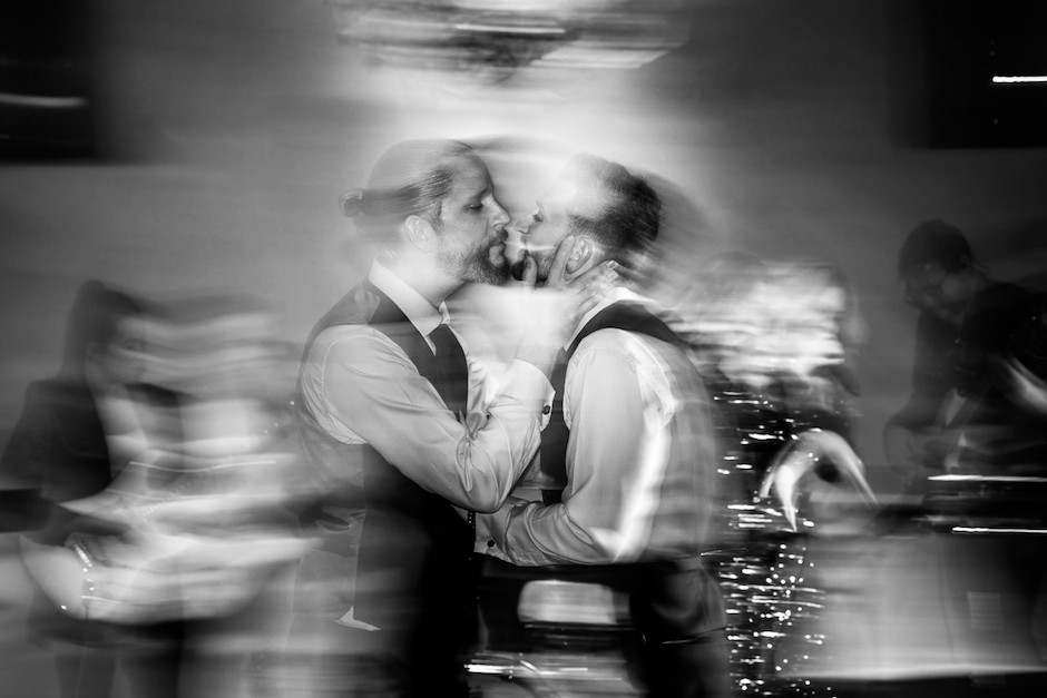 Two grooms embrace at wedding with movement in scene