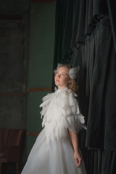 A girl in feather costume behind curtain.