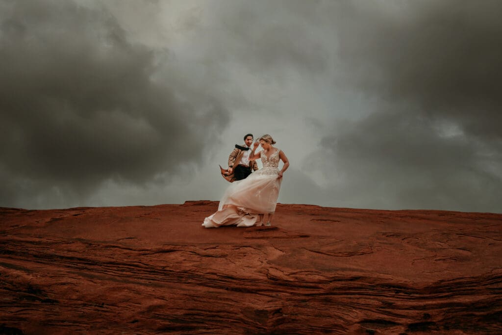 wedding day moments of bride and groom in wind and clouds in desert.