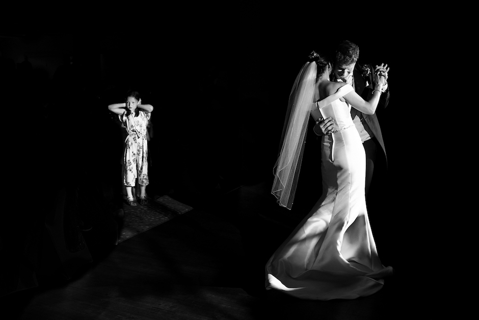 bride and groom dancing with girl holding her hands to her ears in corner of frame.